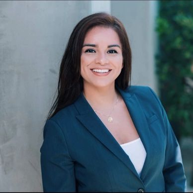 Young woman in a blue blazer smiling confidently outdoors.