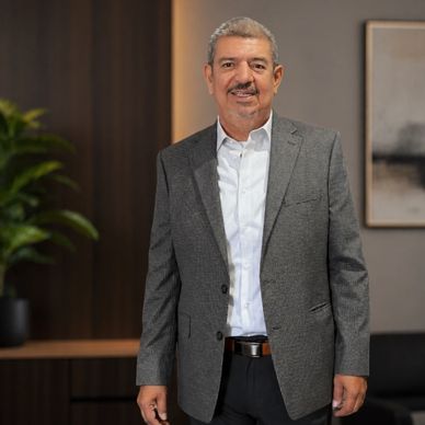 Man in a gray blazer and white shirt standing indoors, smiling.