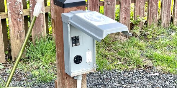 Close-up view of an electrical and water hookup with a fence behind it.