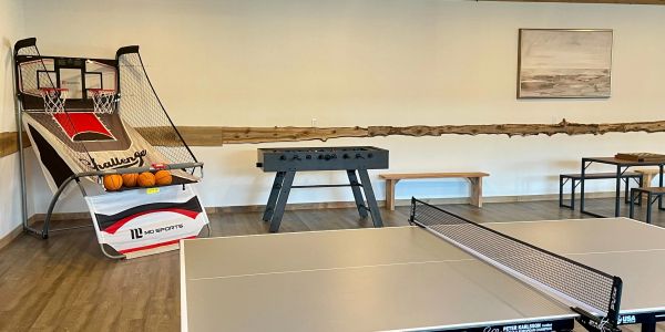 Image inside the clubhouse with a ping pong table, foosball table, and an arcade basketball game.