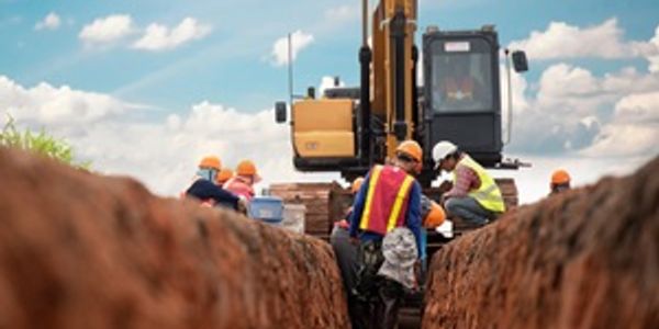 Construction workers in safety gear working in a trench with heavy machinery nearby.