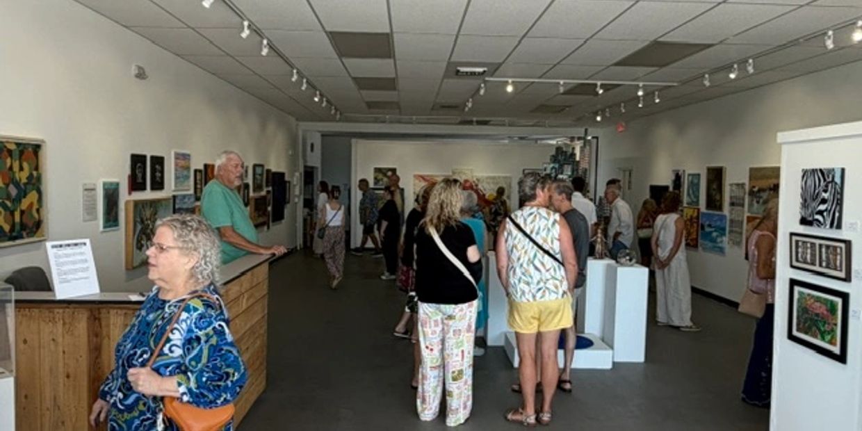 People viewing art in a brightly lit gallery with paintings on the walls.