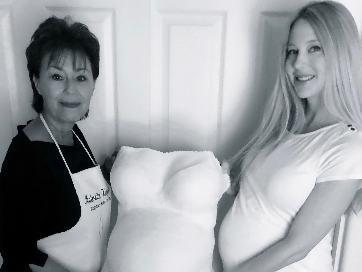 Two women holding a plaster cast of a pregnant belly and chest.