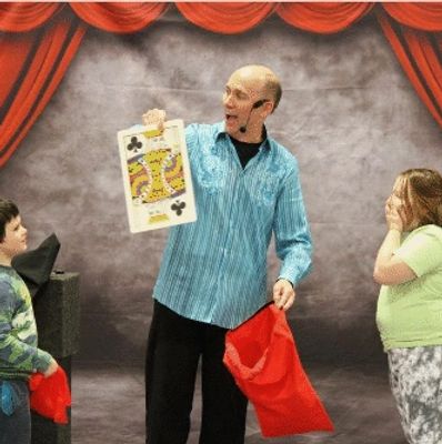 Marty the Magician with a giant playing card and two children looking on with amazed expressions.