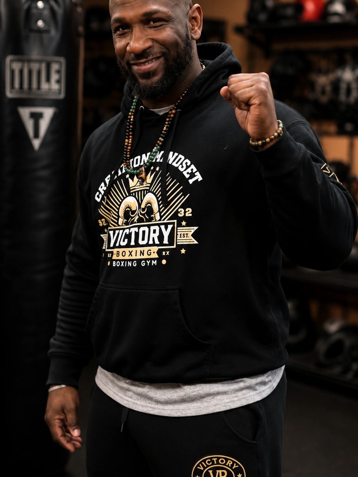 Smiling man in boxing gym wearing Victory hoodie and holding up fist.