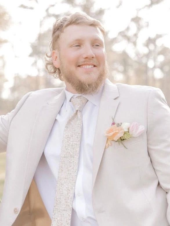 Man in a beige suit smiling outdoors.