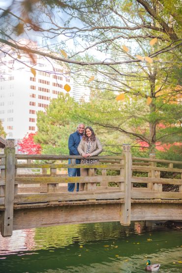 Couple on a wooden bridge in a park with autumn foliage.
