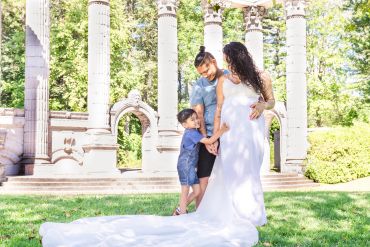 Family outdoors with pregnant mother in white dress.