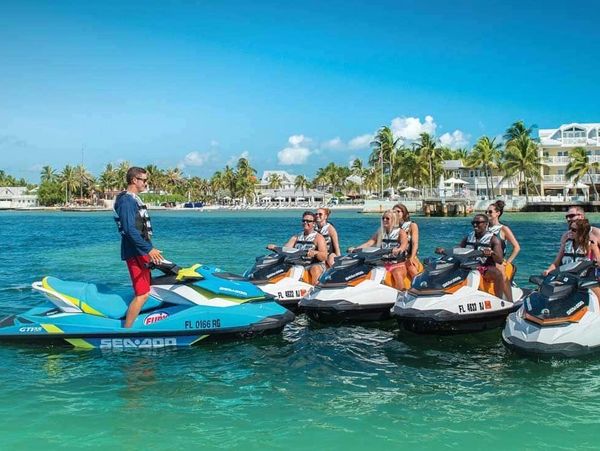 A group on jet skis receiving instructions on clear blue waters.