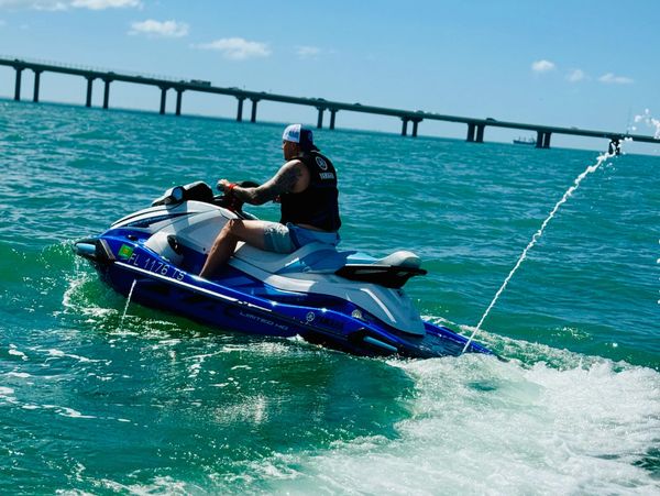Man riding a blue jet ski on clear turquoise water near a bridge.