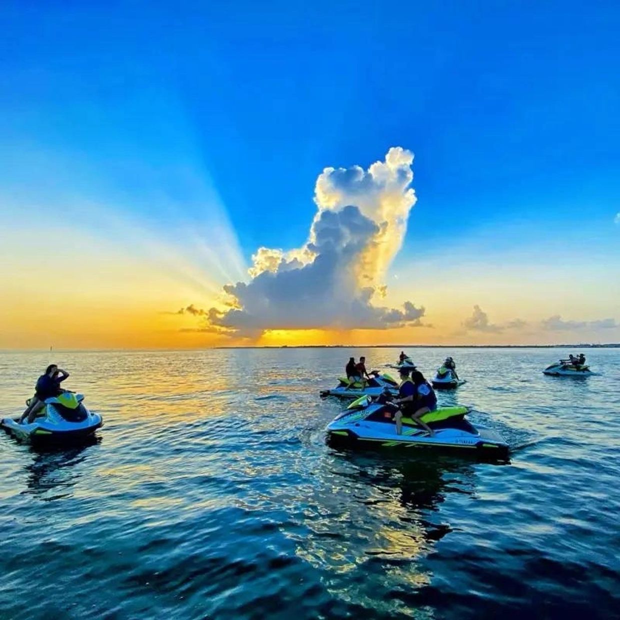 People enjoy jet skiing on calm water during a vibrant sunset with a striking cloud formation.
