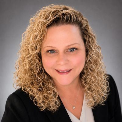 Professional portrait of a smiling woman with curly blonde hair.