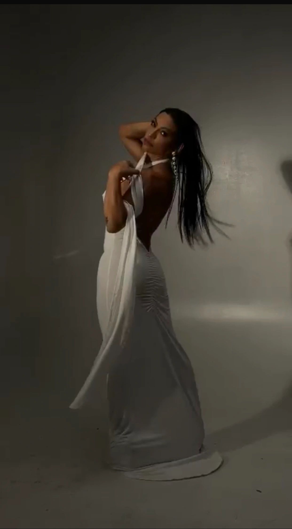 Woman in a flowing white dress poses gracefully against a dark background.