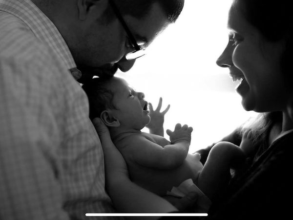 Black and white photo of parents lovingly holding and smiling at their newborn baby.