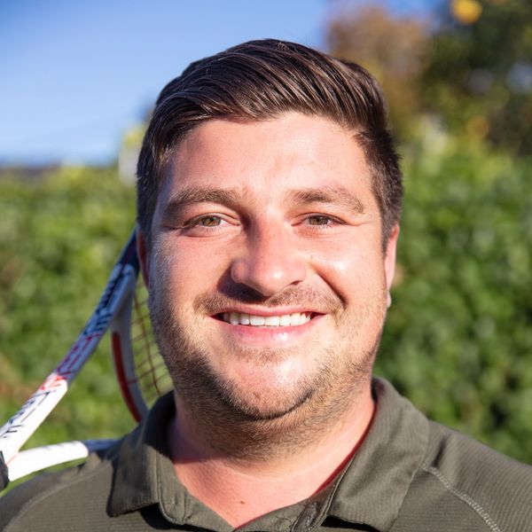 Smiling man with tennis racket outdoors on a sunny day.