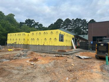 Construction site with a building wrapped in yellow weatherproofing material.