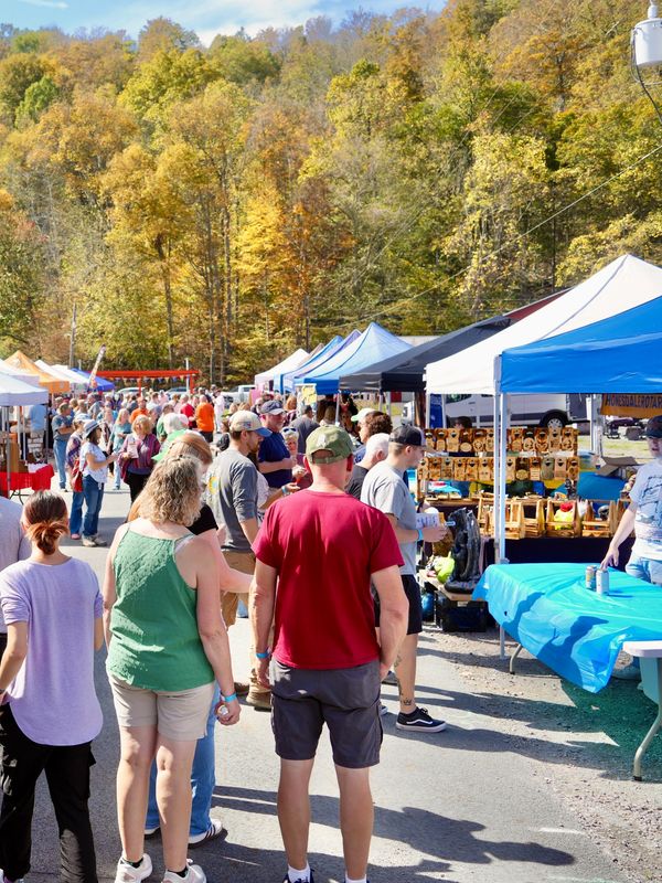 People exploring outdoor market stalls on a sunny autumn day.
