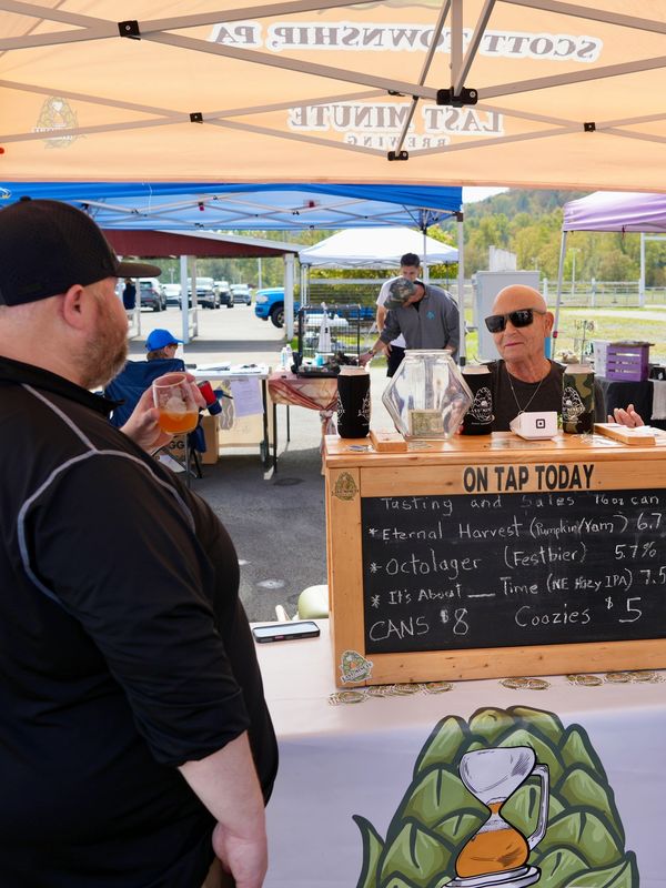 People enjoying a craft beer tasting event at an outdoor booth.