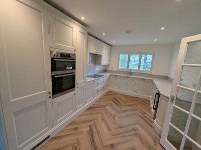 Modern white kitchen with wooden herringbone floor.