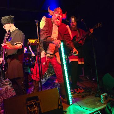 Band performing on stage with a Viking-themed lead singer holding a glowing staff.