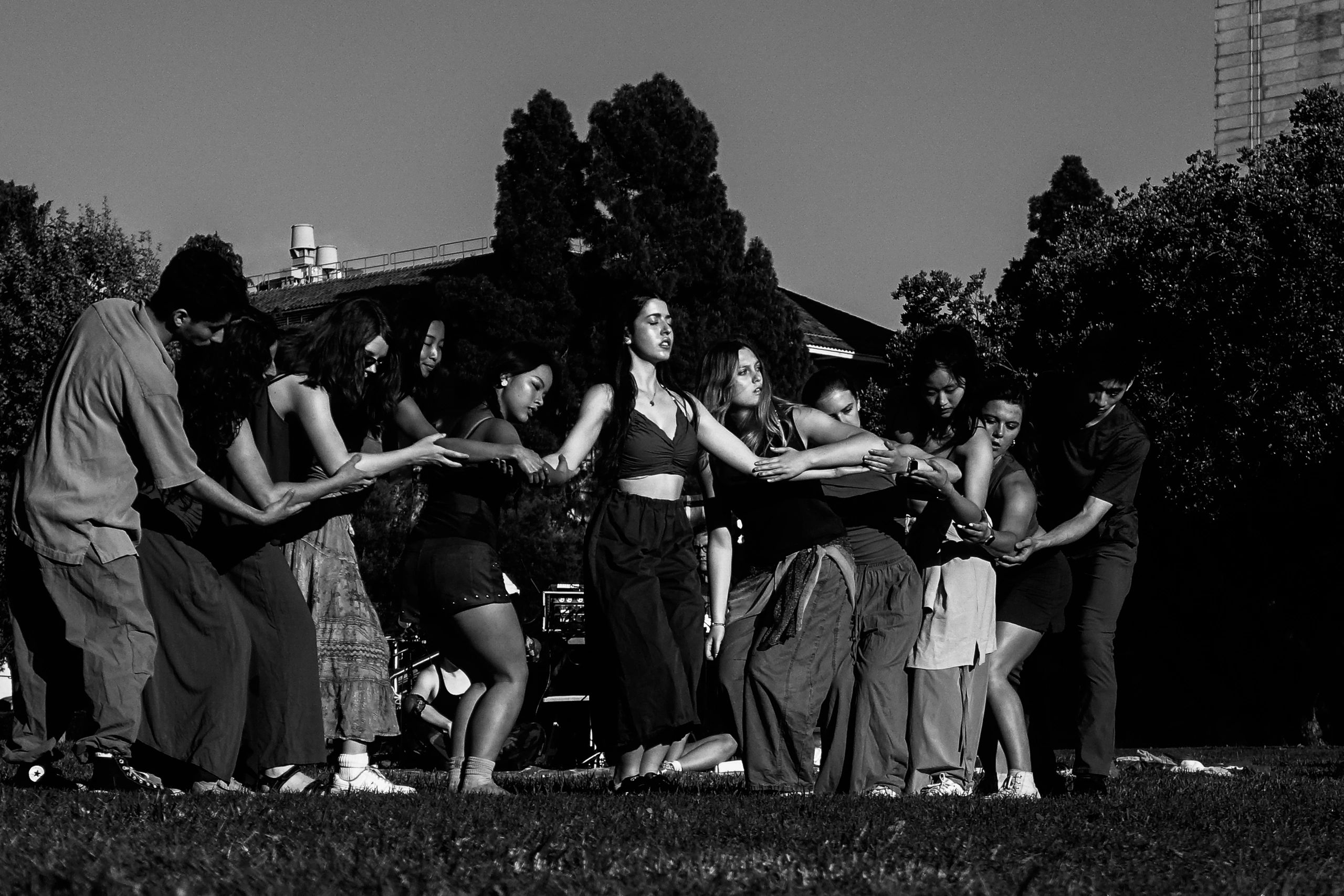 A group of people performing a synchronized outdoor dance in black and white.
