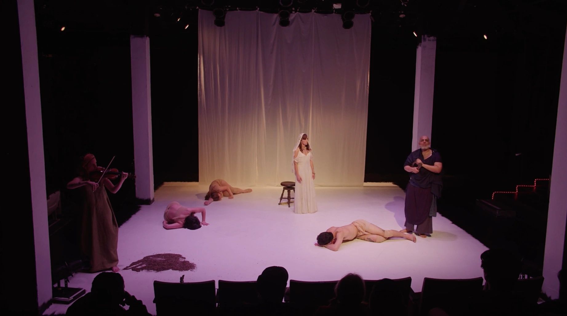 A dramatic stage scene with performers in varied poses and costumes under warm lighting.