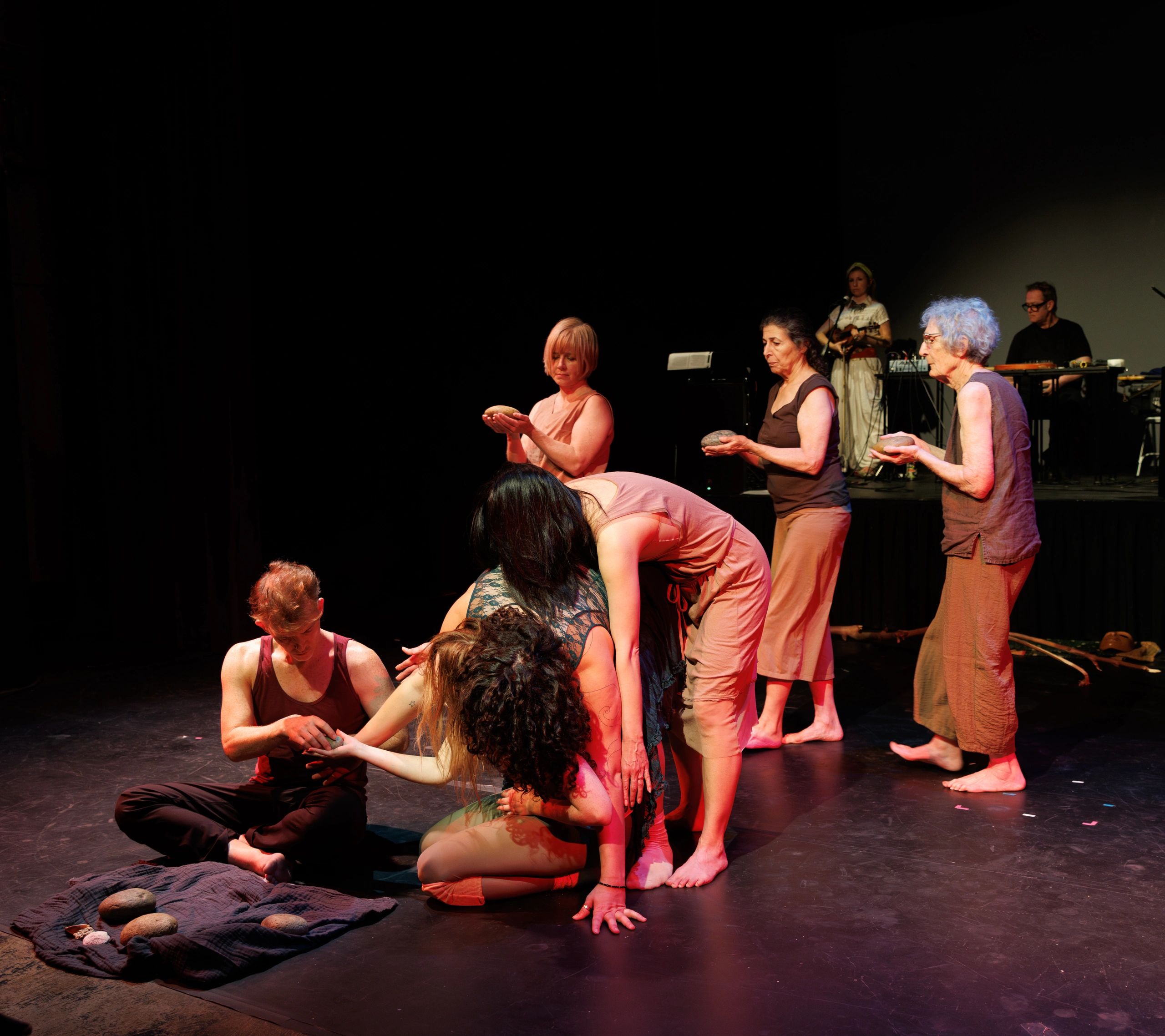Performers holding stones in a dramatic stage setting with musicians in the background.
