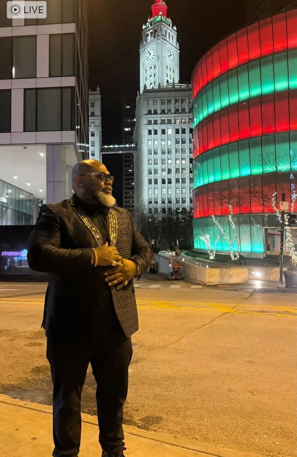 Man in a stylish suit standing on a city street at night with colorful buildings behind.
