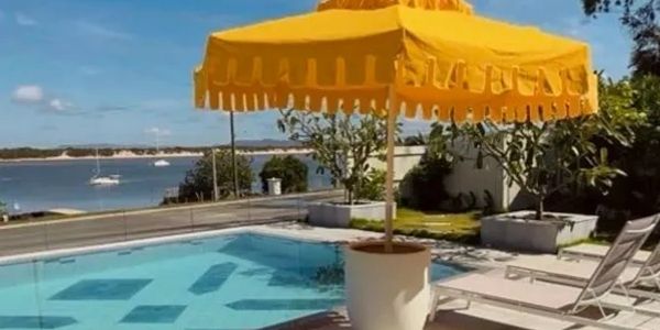 Poolside with yellow umbrella and ocean view under blue sky.