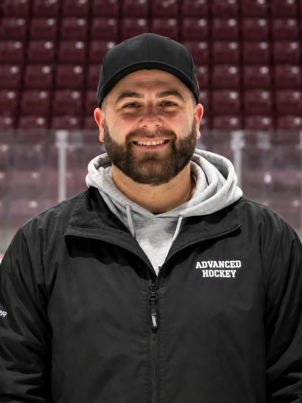 Smiling man in hockey jacket and cap.
