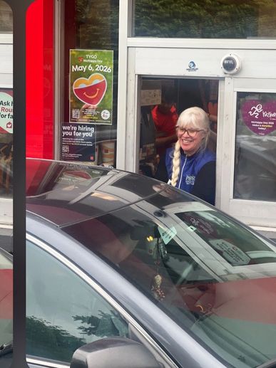 Smiling employee serves a customer through a drive-thru window.