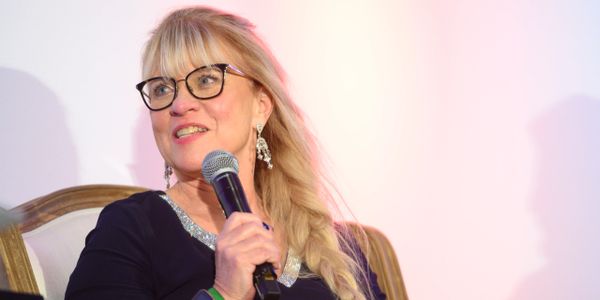 A woman with glasses speaking into a microphone at an event.