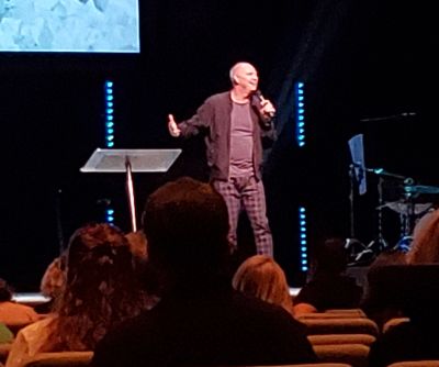 A man speaking on stage to an audience in a dimly lit room.