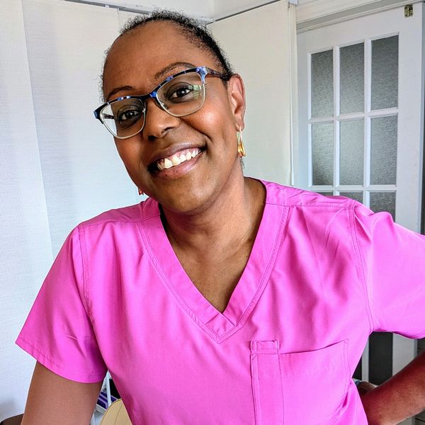 Smiling woman in pink medical scrubs and glasses.