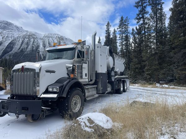 A large white Kenworth truck in a snowy mountainous forest.