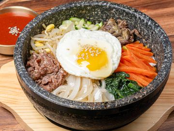 I hot stone bowl filled with rice and assorted vegetables and beef. Gochujang sauce on the side.