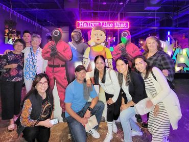 A group of smiling people standing in front of neon lights that read, "Hallyu Like That."