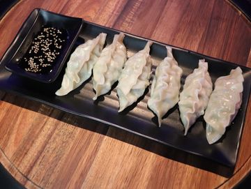 Six steamed dumplings plated alongside soy sauce.