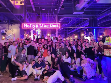 A large group of people posing in front of the Hallyu neon lights that read, "Hallyu Like That."