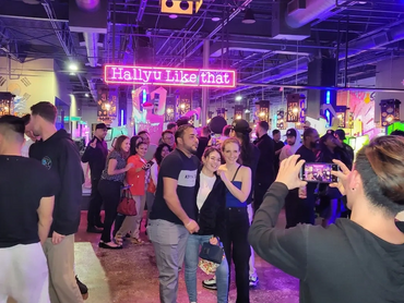A large group of people standing, walking and taking pictures near the restaurant entrance and bar.