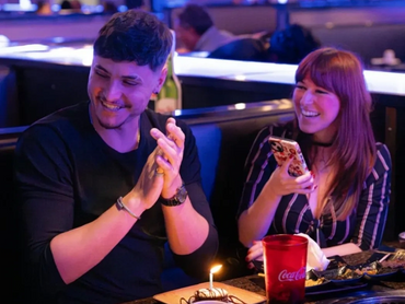 Two people smiling at their table while being served a small complimentary birthday cake.