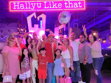 A large group of smiling people standing in front of neon lights that read, "Hallyu Like That."