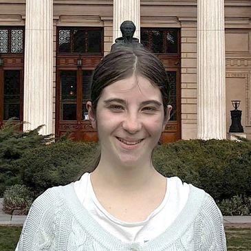 Young woman smiling outdoors in front of a building with columns.