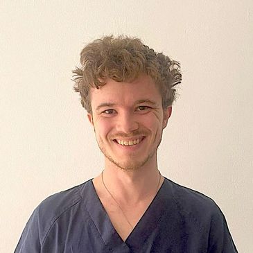Smiling young man with curly hair in dark scrub top.