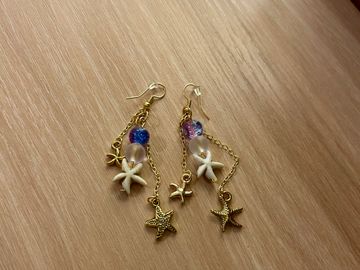 Dangling earrings with starfish charms and colorful beads on a wooden surface.