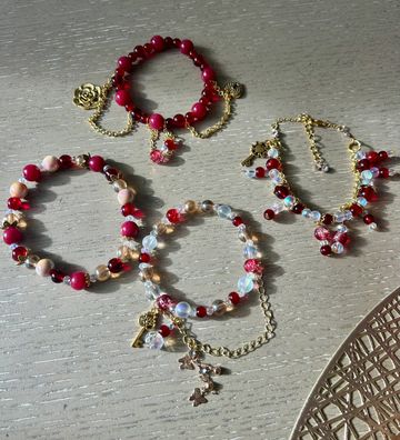 Four colorful beaded bracelets with gold charms on a wooden surface.