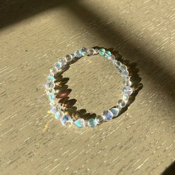 A beaded bracelet glows with iridescent light on a wooden surface.