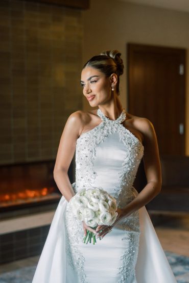 Bride in elegant white wedding gown holding white roses.