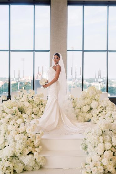 Bride in white dress surrounded by white flowers.