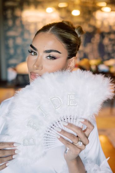 Woman holding a white feathered fan with 'BRIDE' written on it.